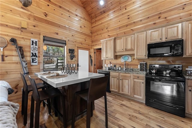 kitchen featuring black appliances, wood walls, light brown cabinets, and a center island