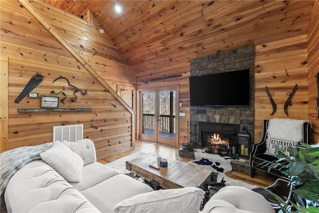 living room with wooden walls, wood ceiling, wood finished floors, a stone fireplace, and french doors