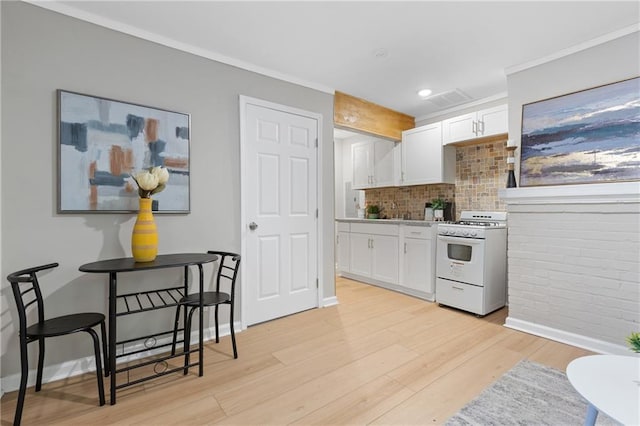 kitchen with crown molding, white gas range oven, white cabinets, light hardwood / wood-style floors, and backsplash