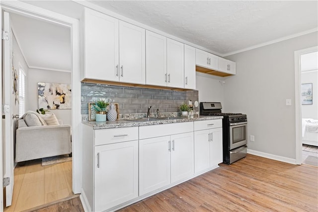 kitchen featuring white cabinetry, sink, stainless steel gas range oven, and light hardwood / wood-style floors