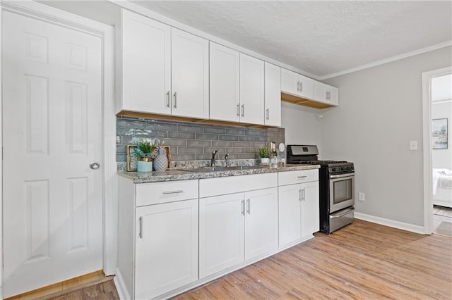 kitchen with sink, backsplash, white cabinets, light hardwood / wood-style floors, and stainless steel range with gas stovetop