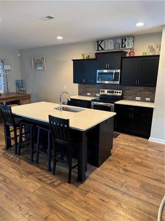 kitchen with a sink, light wood-style floors, a kitchen breakfast bar, appliances with stainless steel finishes, and dark cabinetry