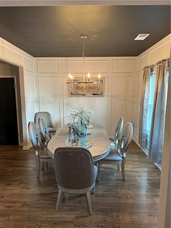 dining space featuring dark wood-type flooring, a notable chandelier, a decorative wall, and visible vents