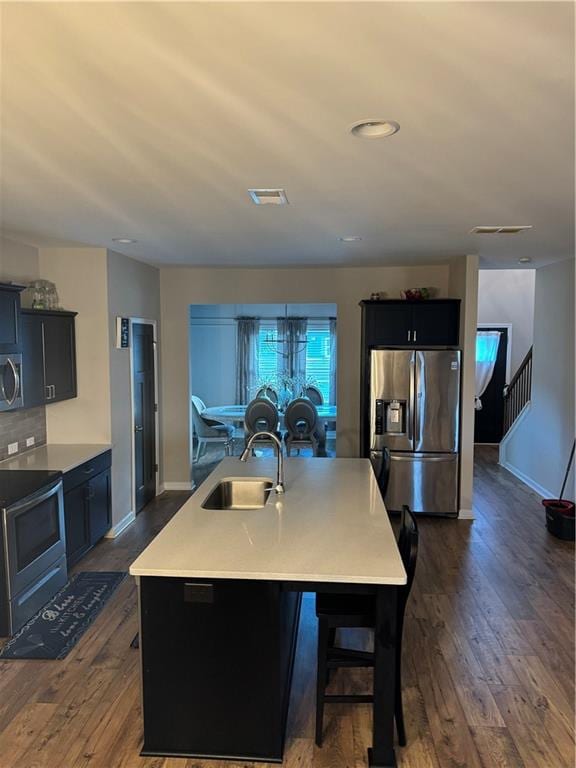 kitchen with dark wood-style flooring, visible vents, appliances with stainless steel finishes, a kitchen island with sink, and a sink