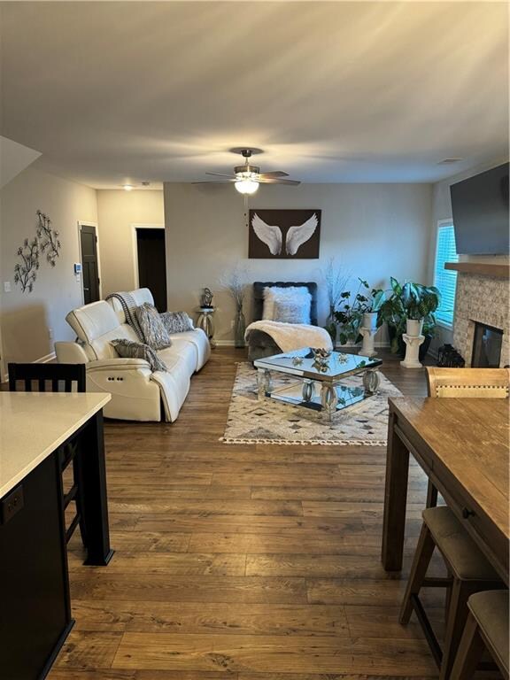 living room featuring wood-type flooring, a glass covered fireplace, and a ceiling fan