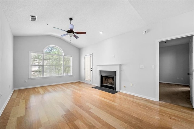unfurnished living room featuring visible vents, ceiling fan, a fireplace with flush hearth, light wood finished floors, and vaulted ceiling