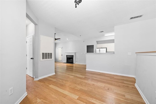 unfurnished living room with light wood-style floors, ceiling fan, a fireplace, and visible vents