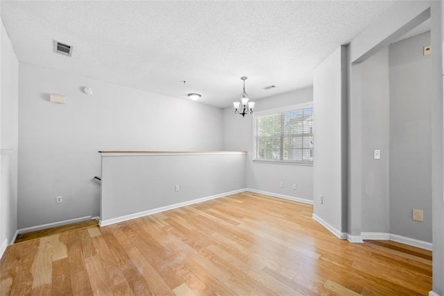 empty room with a textured ceiling, a notable chandelier, visible vents, and light wood-style floors