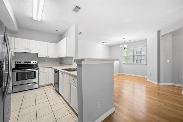 kitchen with a sink, a peninsula, under cabinet range hood, an inviting chandelier, and stainless steel appliances