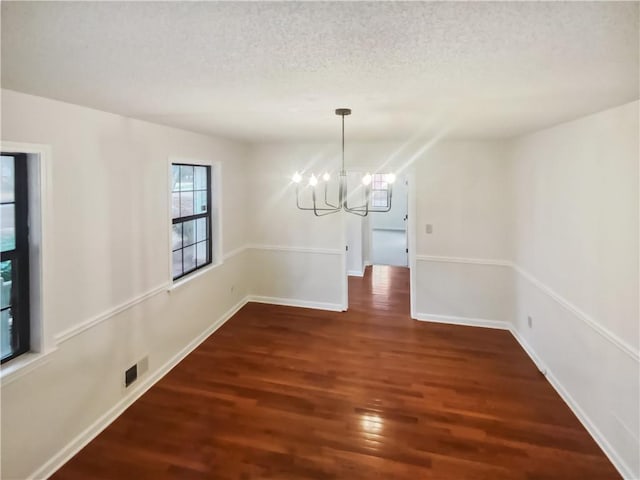 unfurnished dining area featuring dark wood-type flooring, a textured ceiling, and a chandelier