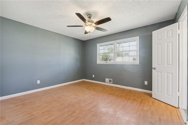 empty room featuring light wood-style floors, visible vents, a textured ceiling, and baseboards