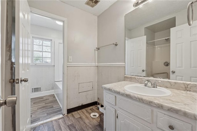 full bath featuring wood finished floors, vanity, visible vents, tile walls, and wainscoting