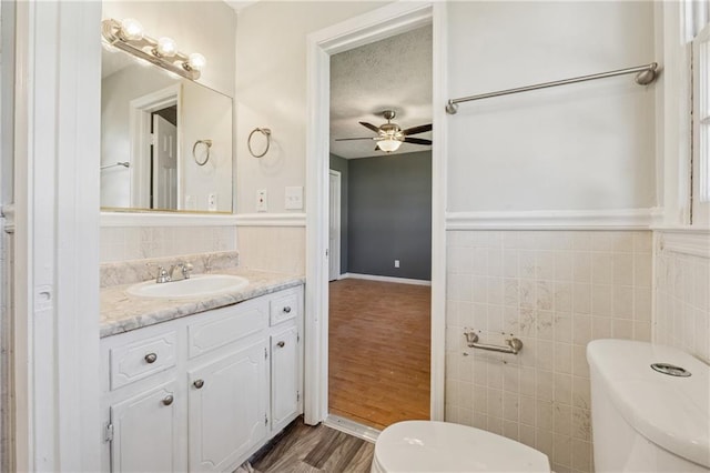 half bath featuring ceiling fan, toilet, wood finished floors, vanity, and tile walls