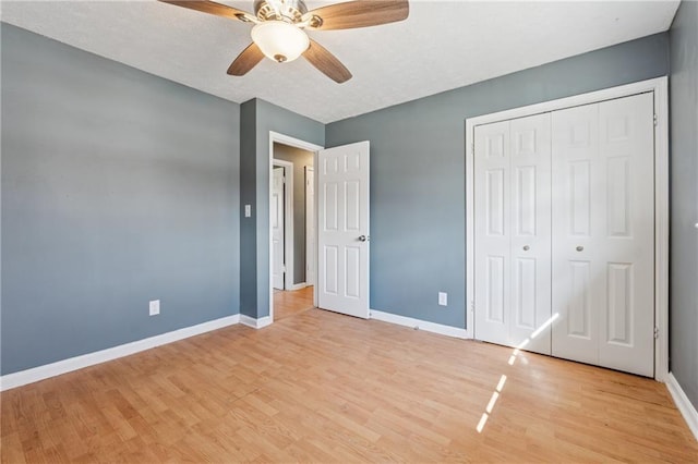 unfurnished bedroom featuring a ceiling fan, light wood-style flooring, baseboards, and a closet