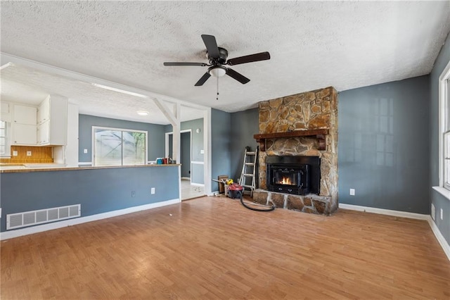 unfurnished living room featuring a fireplace, visible vents, a textured ceiling, wood finished floors, and baseboards