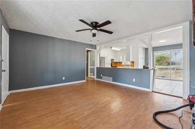 unfurnished living room with baseboards, visible vents, ceiling fan, wood finished floors, and a textured ceiling