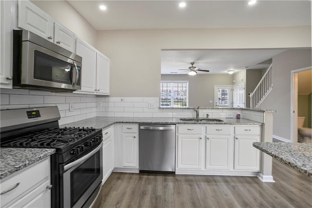 kitchen featuring wood-type flooring, sink, white cabinets, appliances with stainless steel finishes, and light stone counters