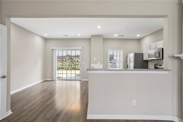 kitchen featuring dark wood-type flooring, kitchen peninsula, stainless steel appliances, white cabinetry, and light stone counters