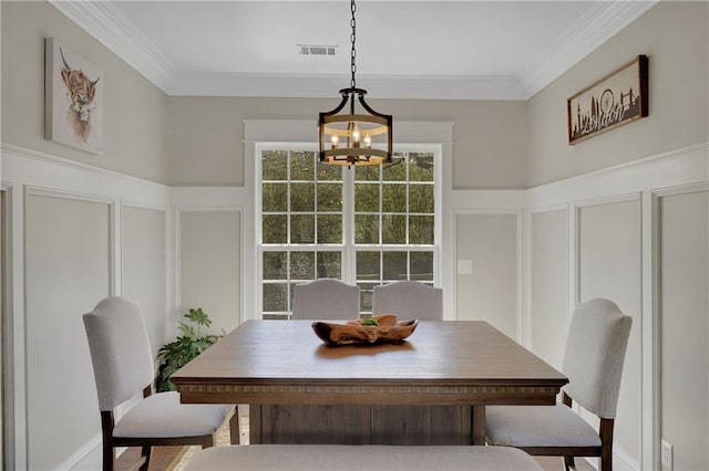 dining space with a chandelier, a decorative wall, wainscoting, and crown molding