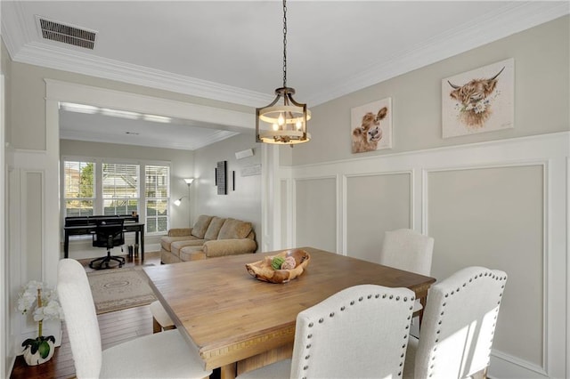 dining room featuring visible vents, ornamental molding, wood finished floors, wainscoting, and a decorative wall