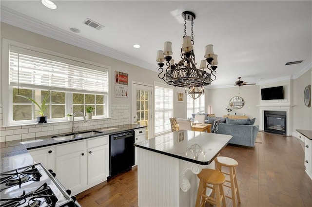 kitchen featuring visible vents, black dishwasher, ornamental molding, a glass covered fireplace, and a sink