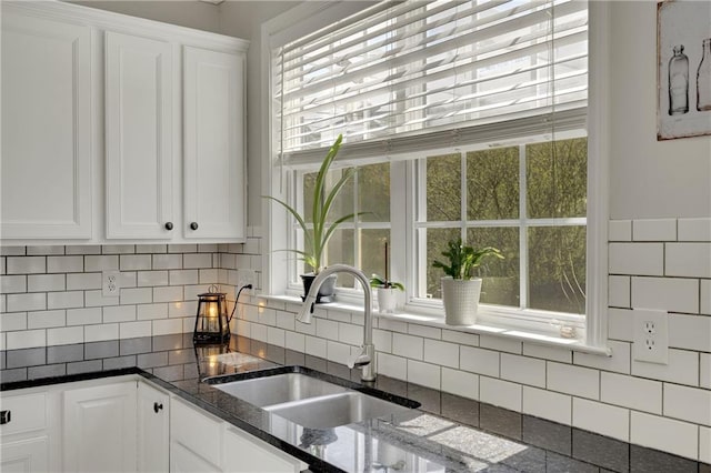 kitchen featuring a sink, decorative backsplash, dark stone countertops, and white cabinetry