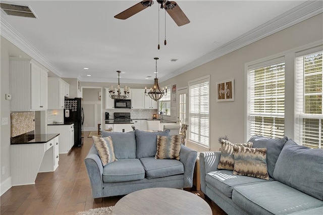 living room featuring visible vents, dark wood-type flooring, ornamental molding, and ceiling fan with notable chandelier