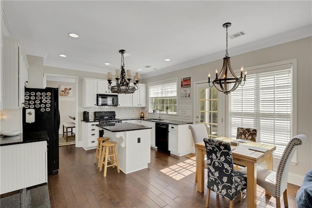 kitchen featuring visible vents, black appliances, dark countertops, a kitchen island, and an inviting chandelier