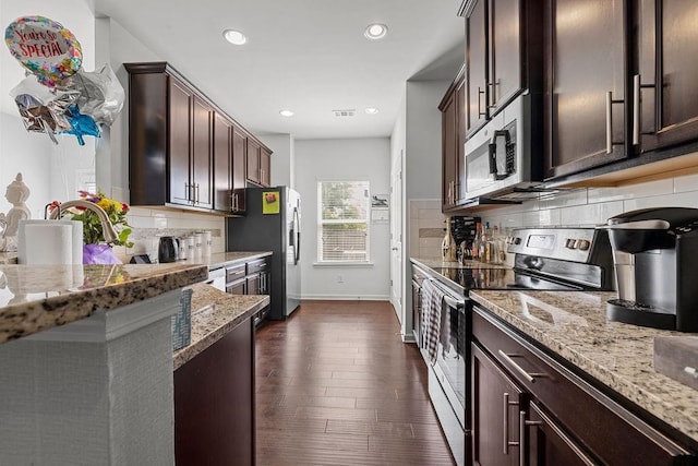 kitchen featuring decorative backsplash, dark brown cabinetry, dark wood-type flooring, appliances with stainless steel finishes, and light stone countertops