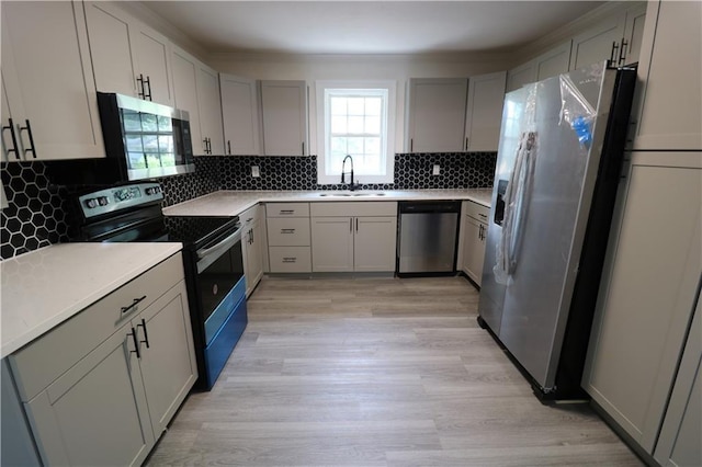 kitchen with light wood-type flooring, tasteful backsplash, stainless steel appliances, sink, and gray cabinets