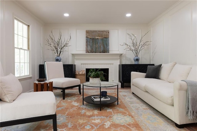 living room featuring a fireplace, recessed lighting, ornamental molding, and a decorative wall