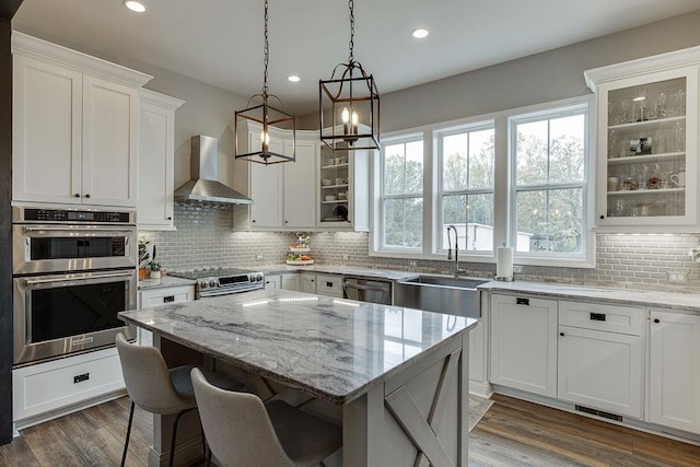 kitchen with wall chimney range hood, a healthy amount of sunlight, white cabinetry, and appliances with stainless steel finishes