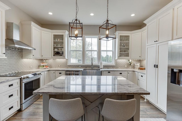 kitchen featuring a kitchen island, wall chimney range hood, appliances with stainless steel finishes, and sink