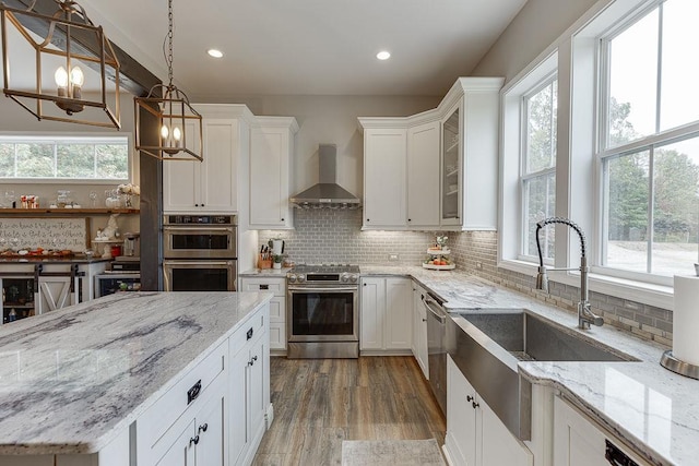 kitchen featuring a wealth of natural light, appliances with stainless steel finishes, wall chimney exhaust hood, and hanging light fixtures