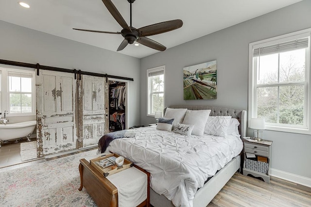 bedroom with light hardwood / wood-style floors, a barn door, ceiling fan, a closet, and a walk in closet