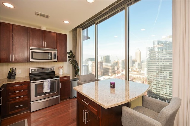 kitchen featuring stainless steel appliances, light stone counters, tasteful backsplash, and dark wood-type flooring