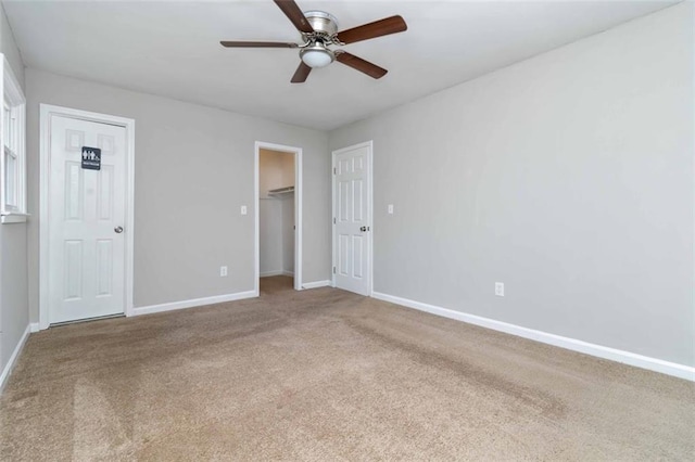 unfurnished bedroom featuring light carpet, a walk in closet, and ceiling fan