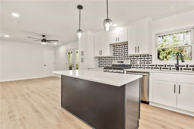 kitchen featuring appliances with stainless steel finishes, white cabinets, a kitchen island, sink, and pendant lighting