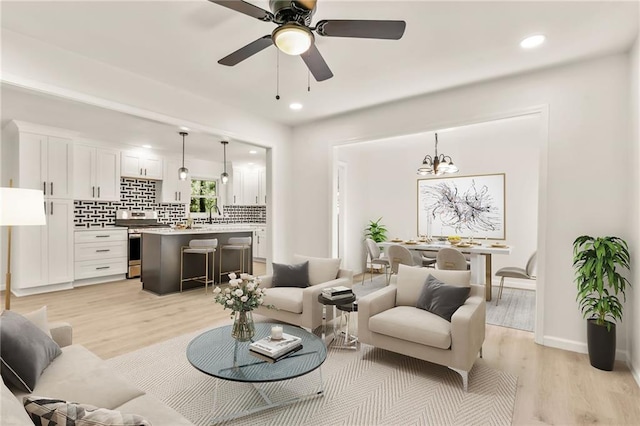 living room featuring light hardwood / wood-style floors, sink, and ceiling fan with notable chandelier