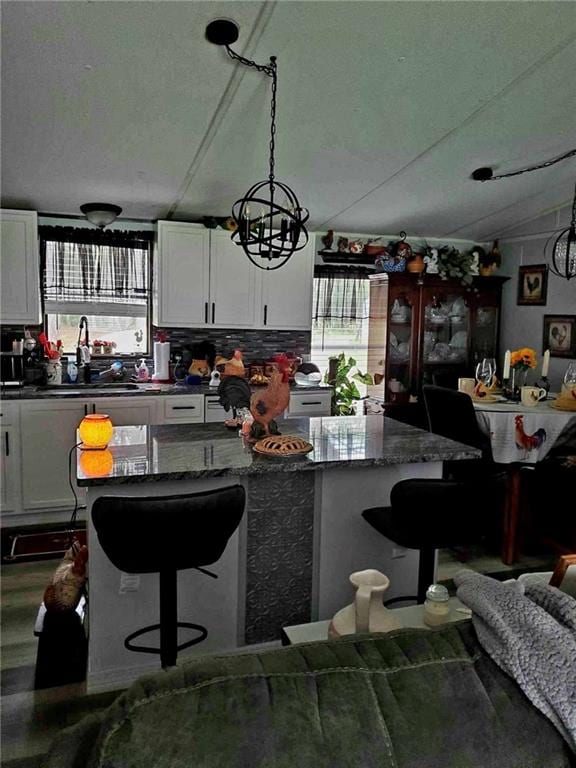 kitchen featuring white cabinetry, hanging light fixtures, a kitchen bar, vaulted ceiling, and dark stone counters