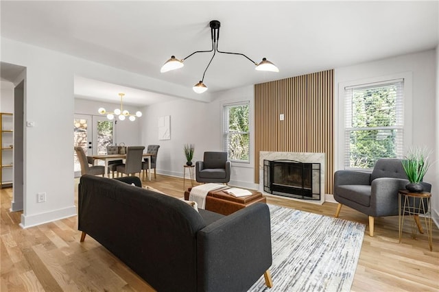 living area with light wood-type flooring, an inviting chandelier, baseboards, and a high end fireplace