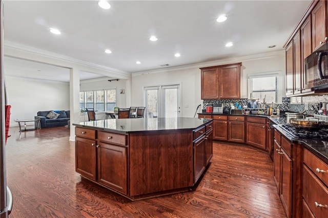 kitchen with black microwave, a kitchen island, open floor plan, decorative backsplash, and dark wood finished floors