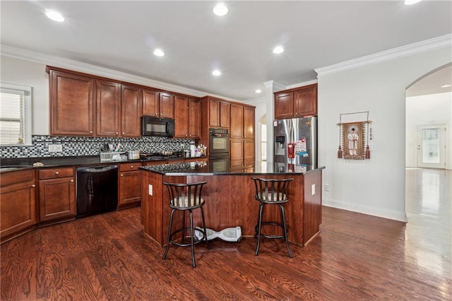 kitchen featuring arched walkways, dark wood-style flooring, a kitchen island, decorative backsplash, and black appliances