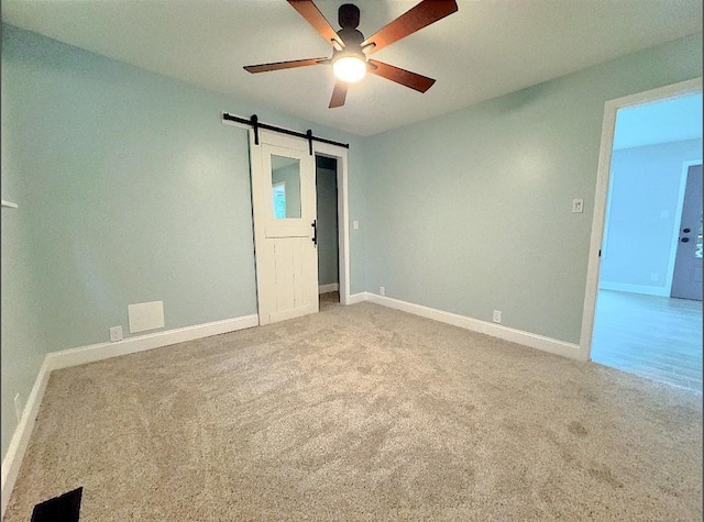 carpeted empty room featuring ceiling fan and a barn door