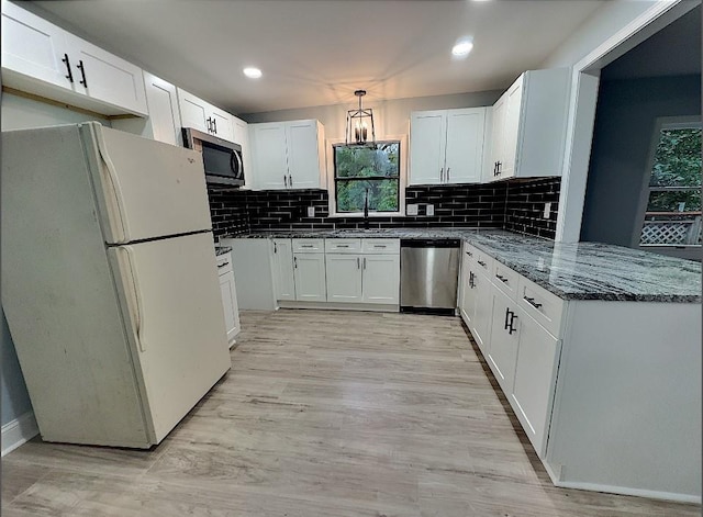 kitchen featuring appliances with stainless steel finishes, dark stone countertops, hanging light fixtures, white cabinets, and sink