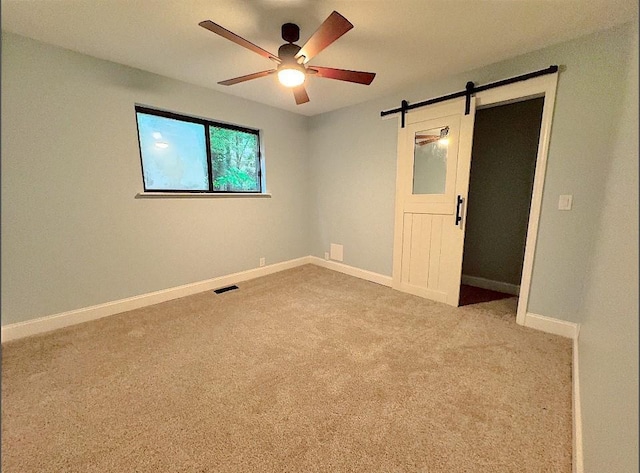 carpeted spare room with ceiling fan and a barn door