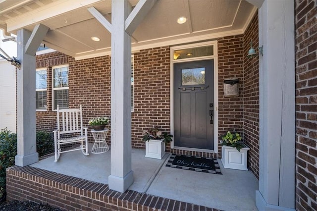 doorway to property featuring brick siding and a porch