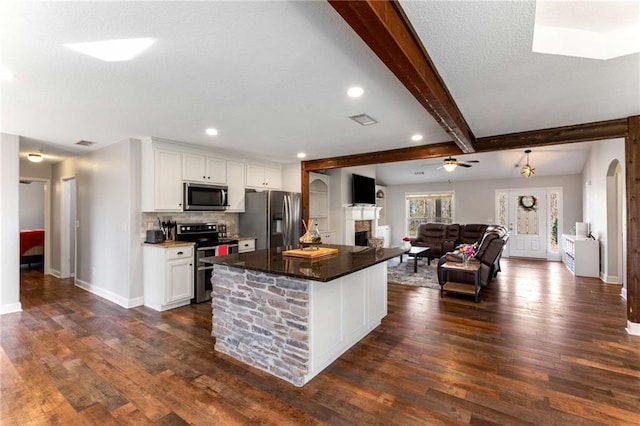 kitchen featuring beam ceiling, white cabinetry, arched walkways, appliances with stainless steel finishes, and a fireplace