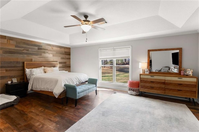 bedroom with visible vents, a ceiling fan, wood finished floors, wood walls, and a raised ceiling