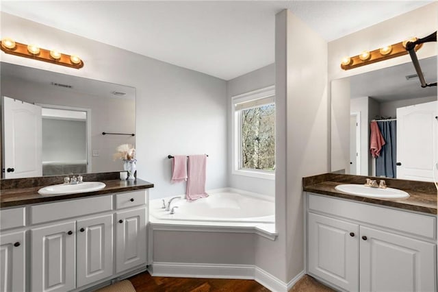 bathroom with a sink, visible vents, a garden tub, and two vanities